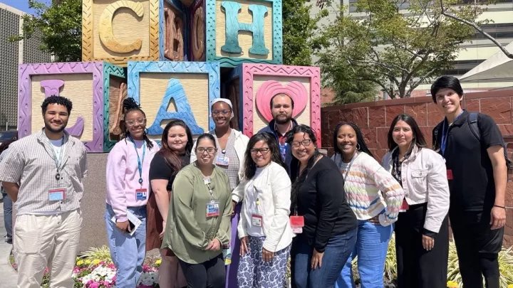 Group of men and women of varying skin tones standing in front of lettered blocks.