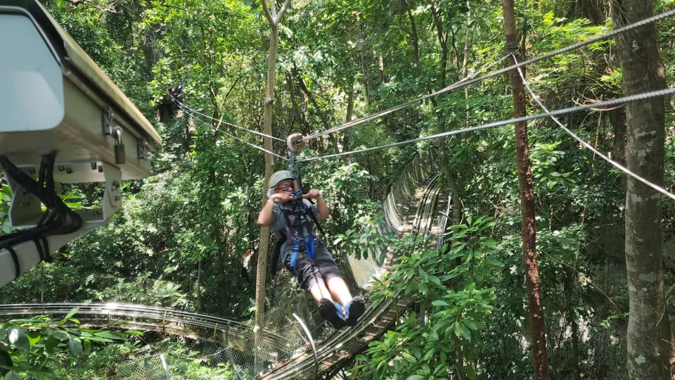 A boy in safety harness and helmet hangs from a zipline