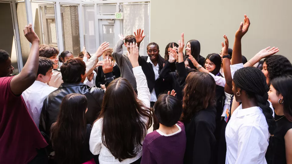 A group of high schoolers stand in a circle put their hands up in unison.