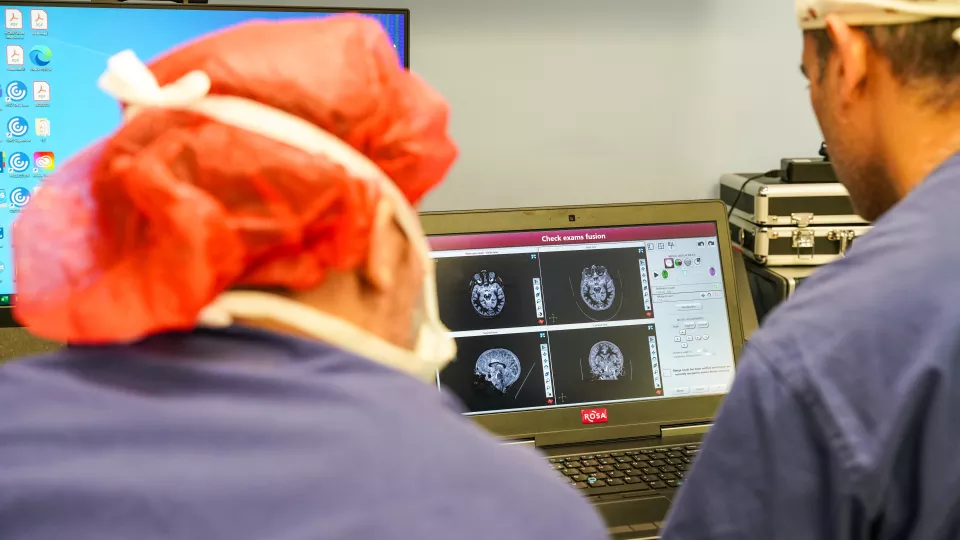 Two physicians look over a laptop screen with MRI scans of a patient's brain.