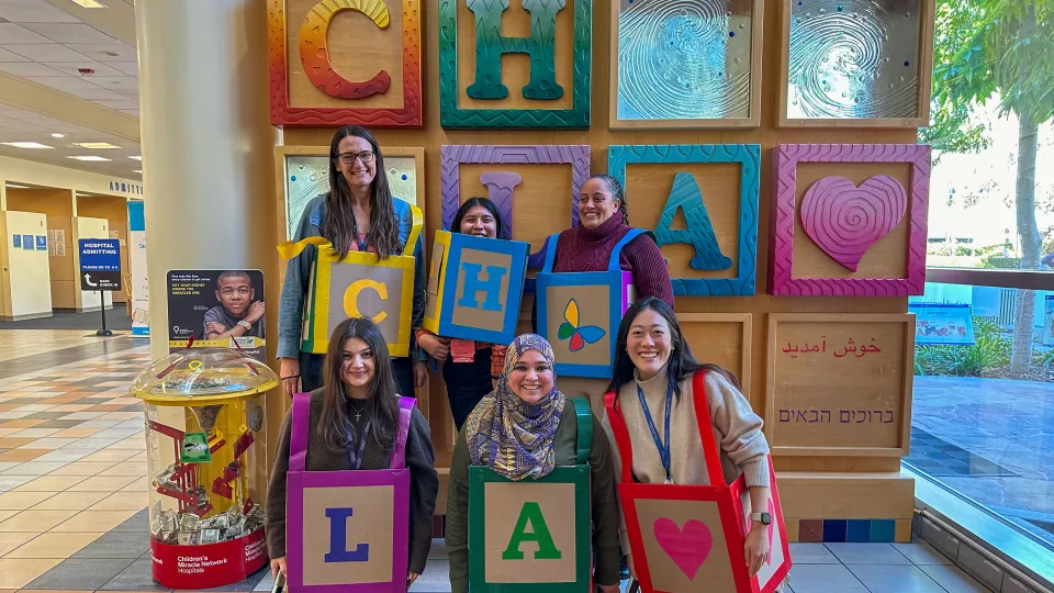 Six team members pose in front of the CHLA blocks art installation dressed up in their homemade CHLA block costumes.