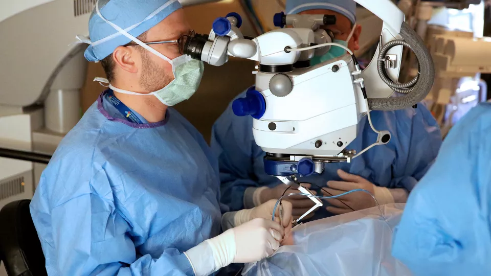 Dr. Aaron Nagiel looks into a microscope during bilateral eye surgery for Luxturna gene therapy.