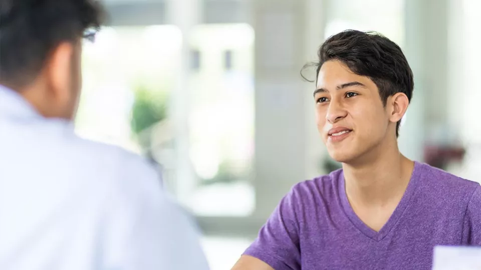 Patient with medium skin tone and dark hair speaks to health care provider in white lab coat