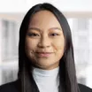 Headshot of a slightly smiling woman with medium skin tone and straight, dark hair wearing a white turtleneck under a dark suit jacket against a neutral indoor background