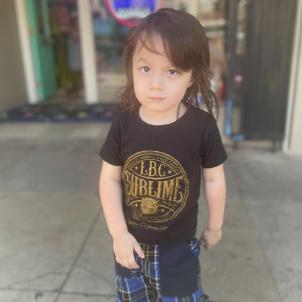 Young boy with medium skin tone and dark hair wearing a black t-shirt and patterned shorts