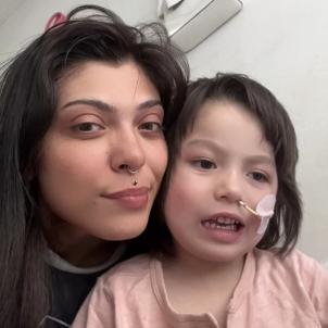 Young mother with medium skin tone and dark hair takes indoor selfie with young son with medium skin tone, dark hair and feeding tube