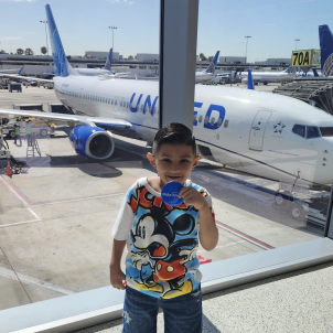 Nano stands in front of an airplane in the terminal of an airport.
