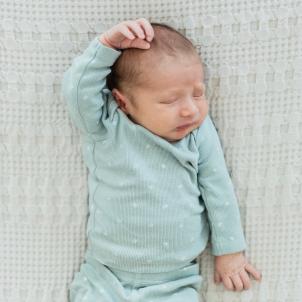 Infant in light blue clothes and eyes closed reaching his right arm and holding left arm down