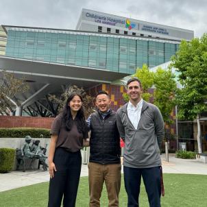 Three adults with various skin tones stand posed together outdoors in front of a building at Children’s Hospital Los Angeles.