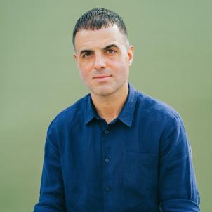 Professional headshot of Josh Zad, CEO of Alfred Coffee wearing a blue collared shirt sitting against a light green background
