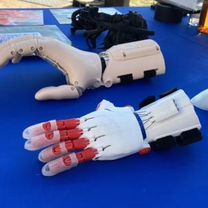 Two different models of 3D-printed prosthetic hands (foreground) and a 3D-printed model of a human heart for presurgical planning (background) are displayed on a table at the CATCH Holiday Party.