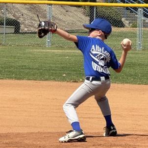 A child with a light skin tone and wearing a blue baseball uniform prepares to pitch a ball.