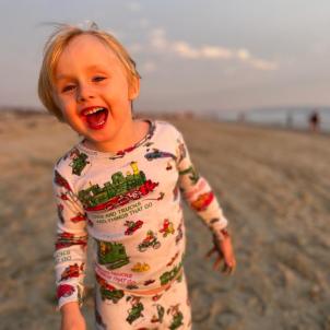 A young boy smiles at the camera on the beach at sunset.